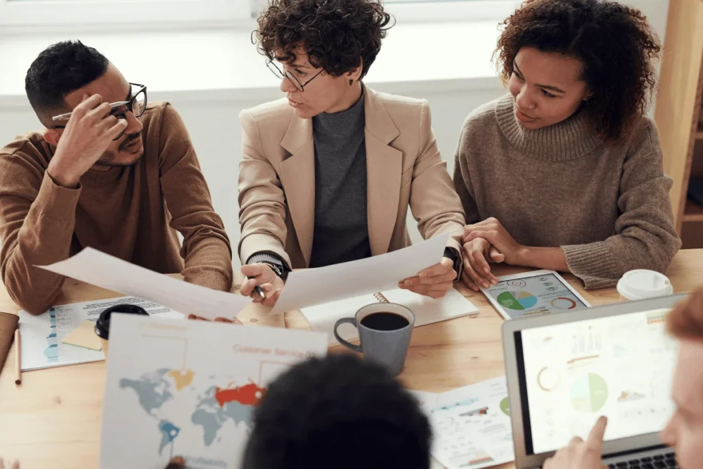 A diverse group of professionals collaborates at a table, reviewing charts and graphs.
