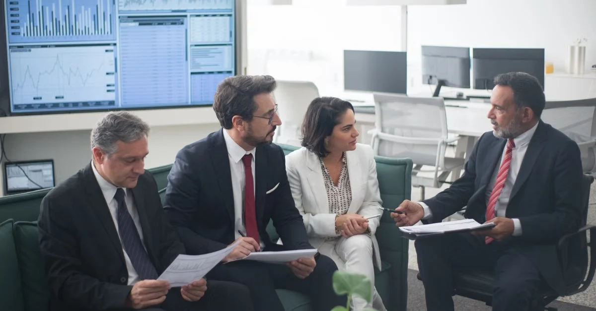 Four professionals in business attire discussing high net worth estate planning documents in modern office with data.