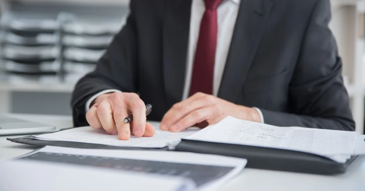 Businessman reviewing transfer pricing adjustment documents at desk in office setting.
