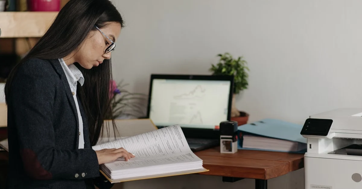Woman in business attire reviewing transfer pricing strategy documents at desk with laptop and office supplies.