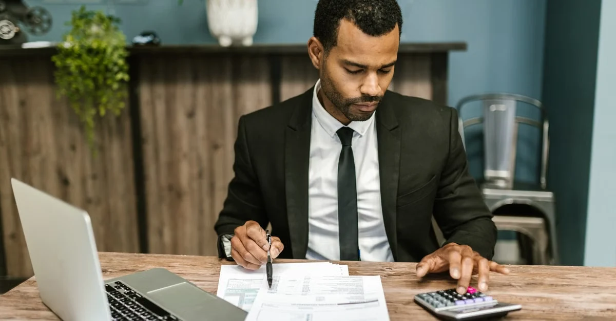 Businessman reviewing bookkeeping services pricing documents at desk with laptop and calculator.