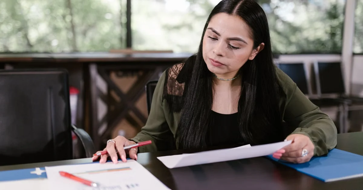 Woman reviewing business exit planning documents and financial charts at desk with focused attention.